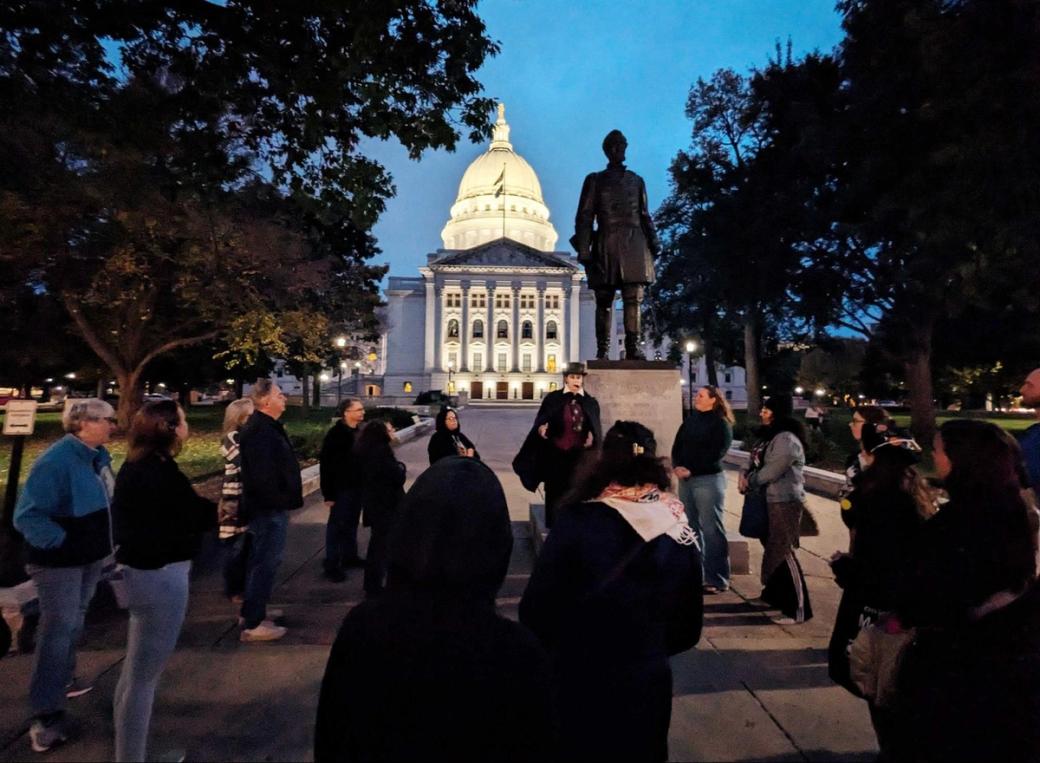 A group of people standing in front of a dome listen to a speaker.