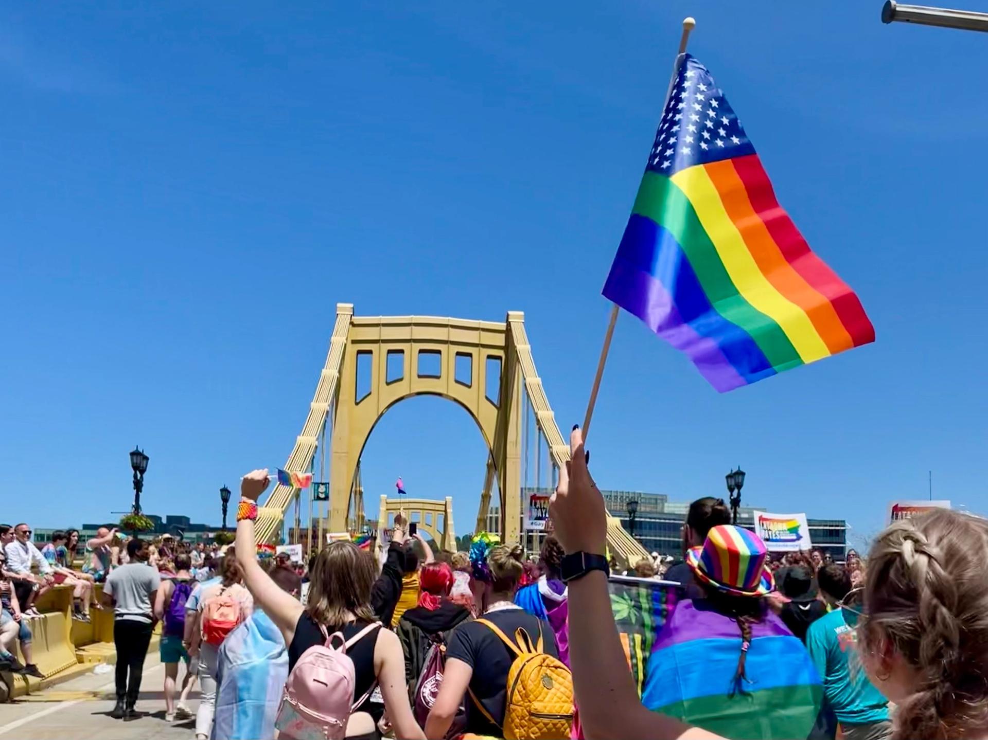 pride flag in front of the Pride parade marching across the Roberto Clemente Bridge