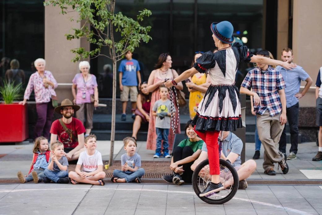 A woman on a tricycle performs in front of children.