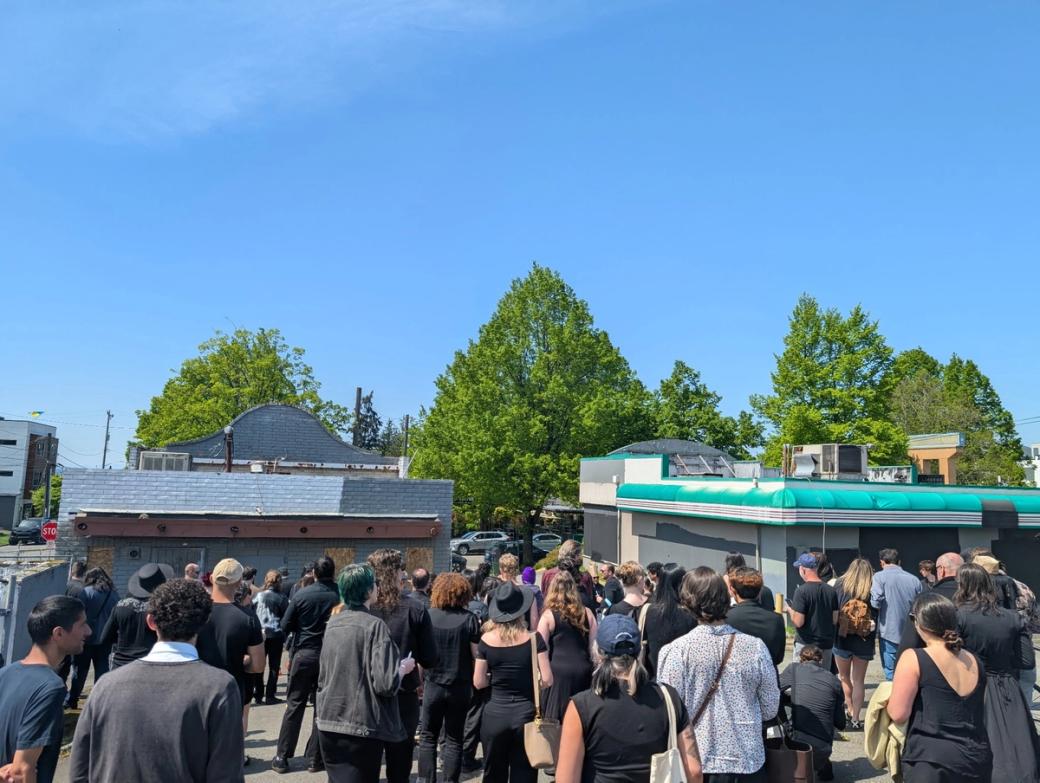 A group of people stand near two empty buildings as part of the ‘Taco Bell Funeral’