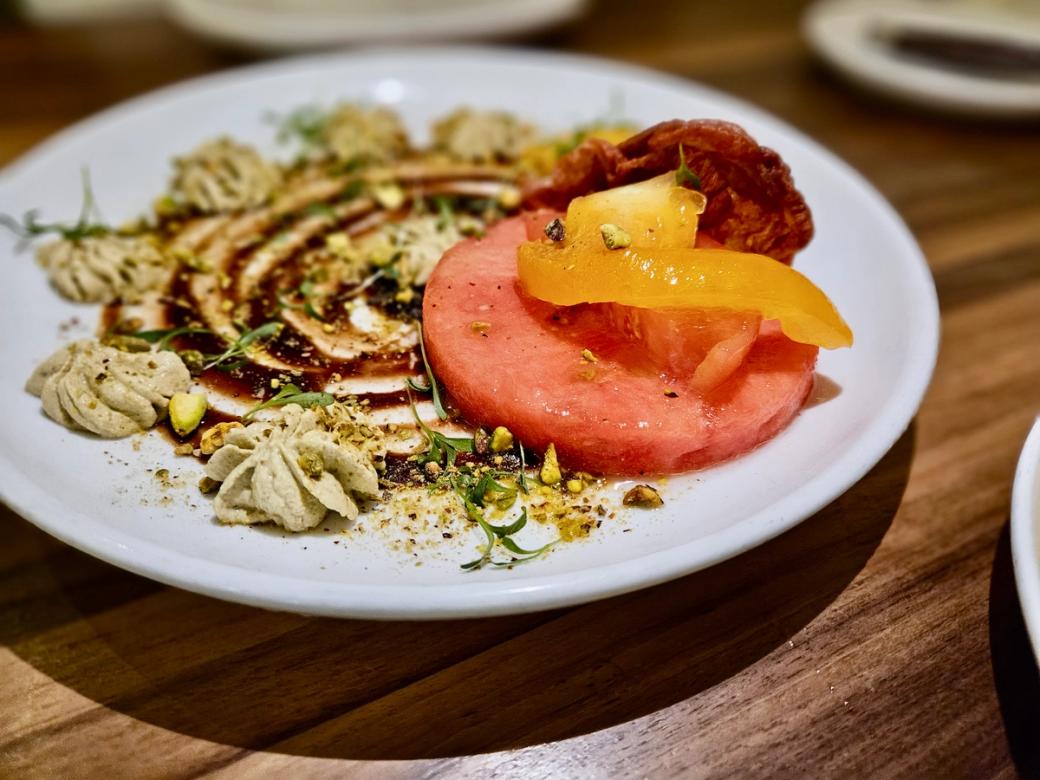 A salad on a white plate with watermelon and pistachios.