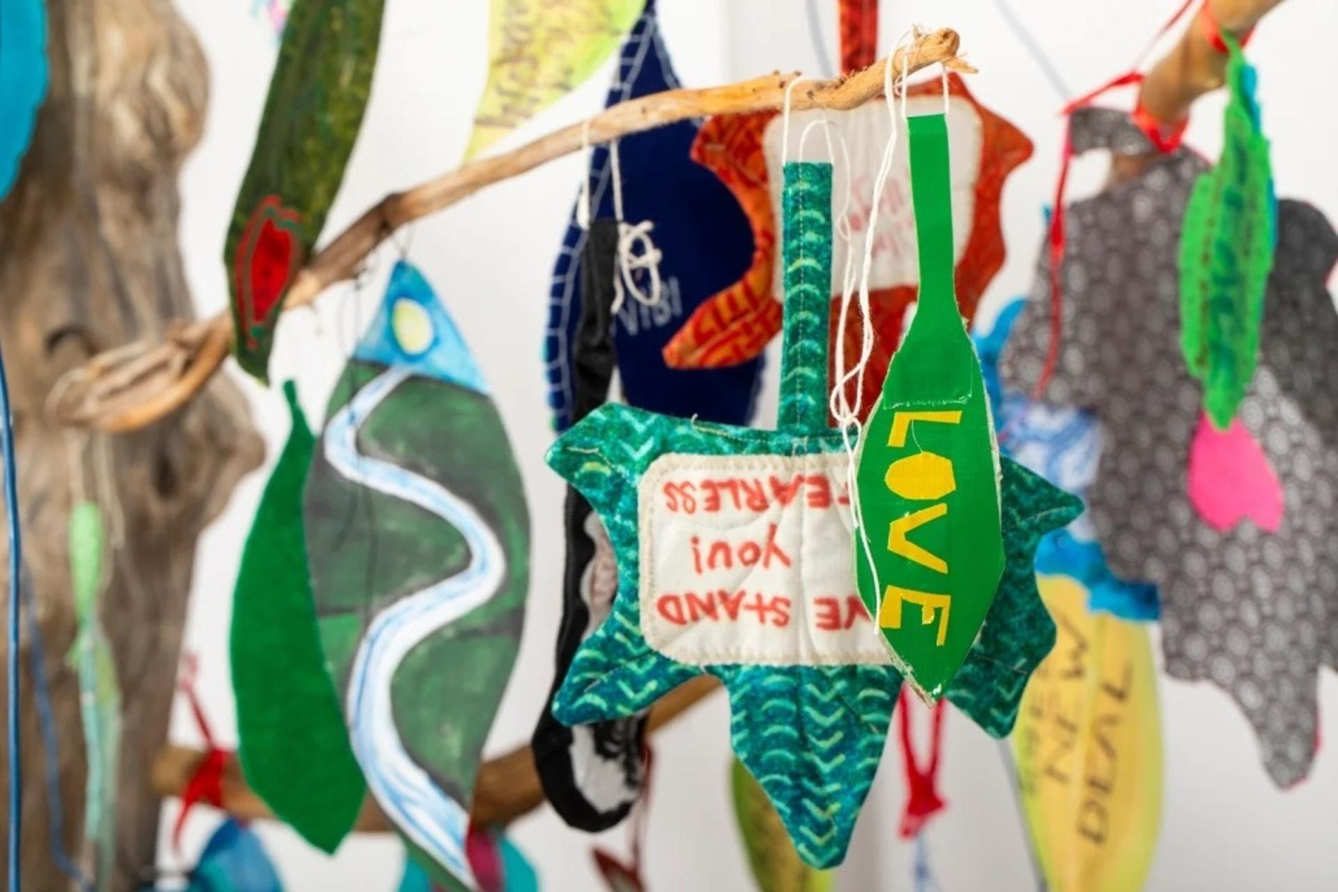 Cloth and paper shaped as leaves are hanging from a manmade branch. One says "love"