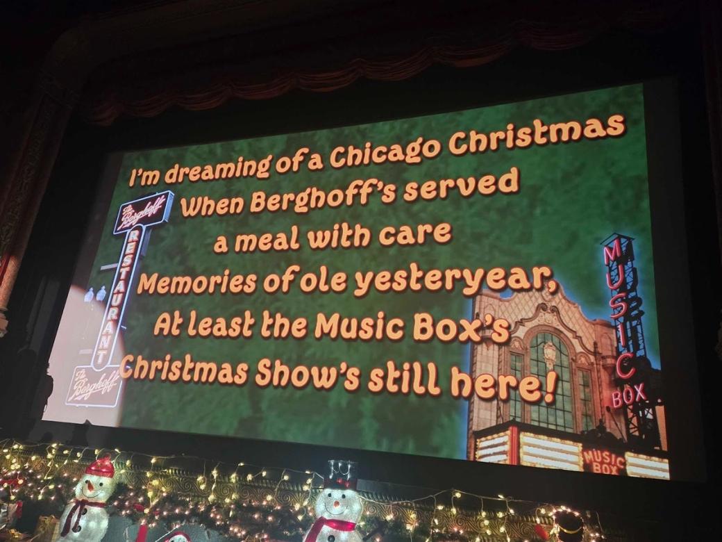 Photo of large screen with lyrics parodying "White Christmas," and Christmas decor beneath the screen