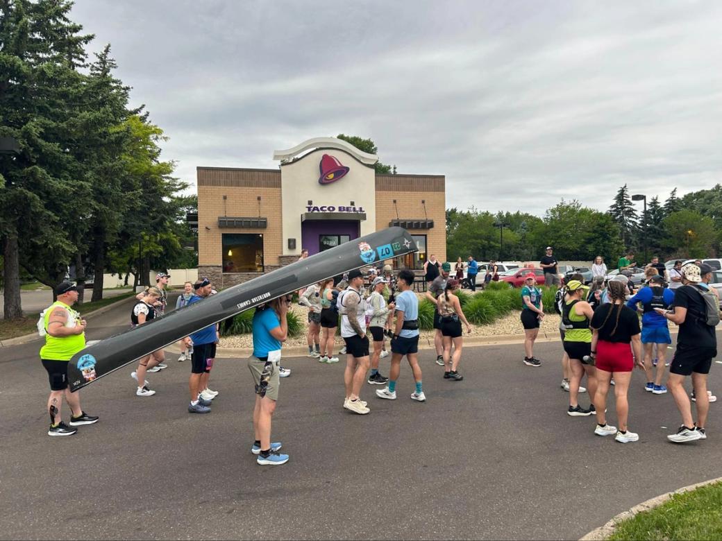 Taco Bell 50k attendees gathered outside the Bloomington location. One is carrying an upside-down canoe balanced on his head.