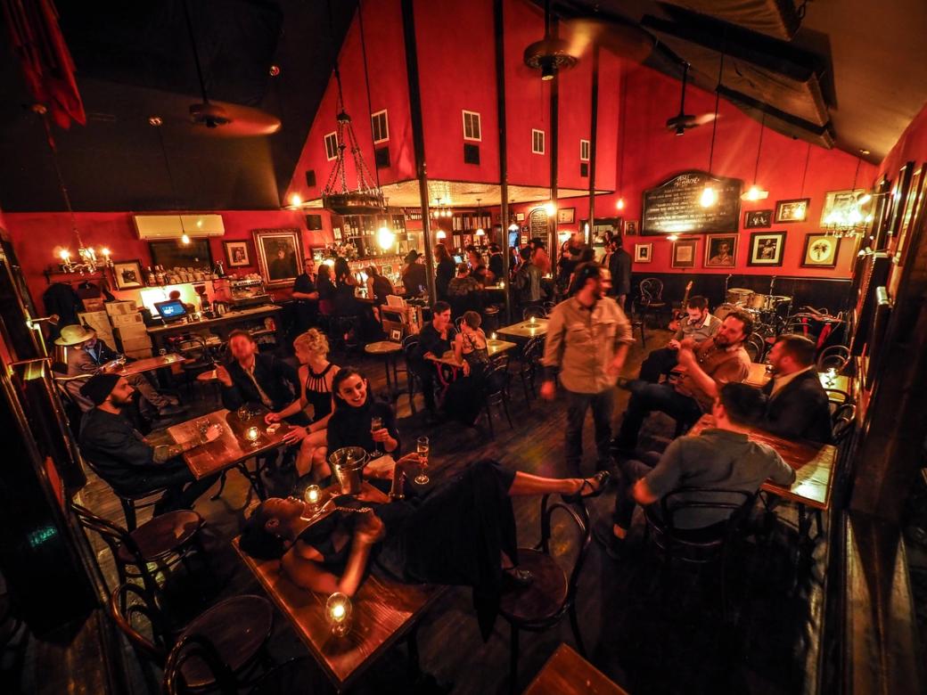 A dark restaurant with red walls and lots of patrons.