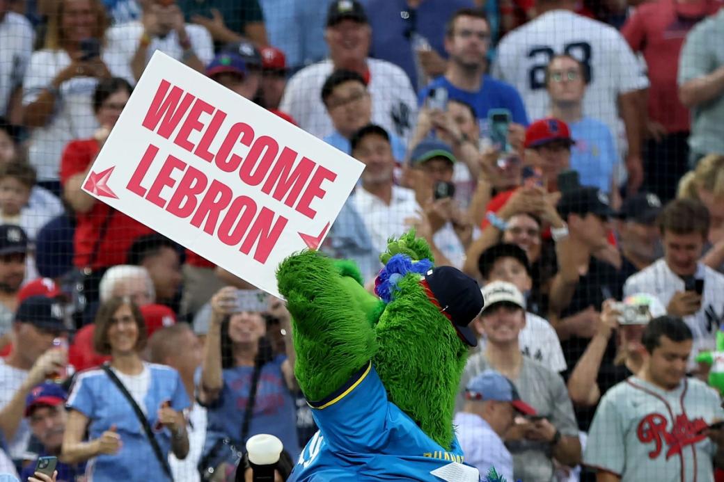 Facing a large crowd of fans, The Phillie Phanatic mascot holds a sign that says "Welcome LeBron."