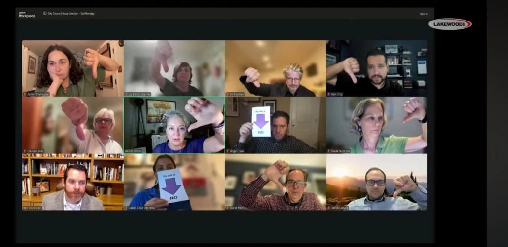 A three-by-four grid of Lakewood City Council members in a Zoom meeting, each holding a thumbs-down pose. 