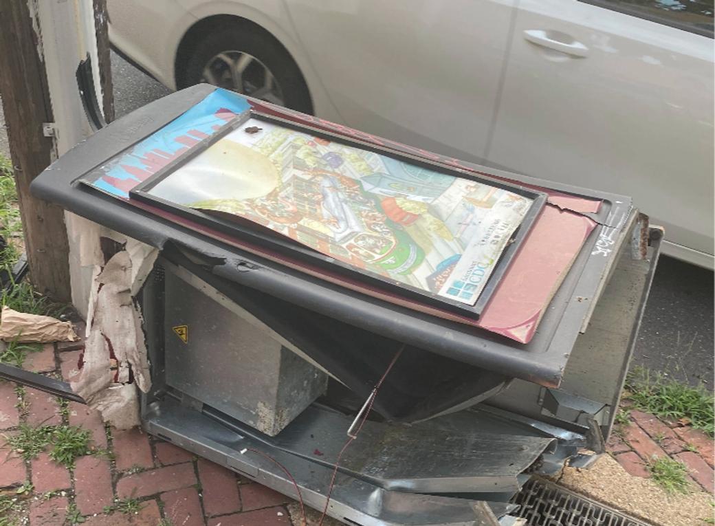 a Big Belly trash can completely smashed and destroyed on a sidewalk. 