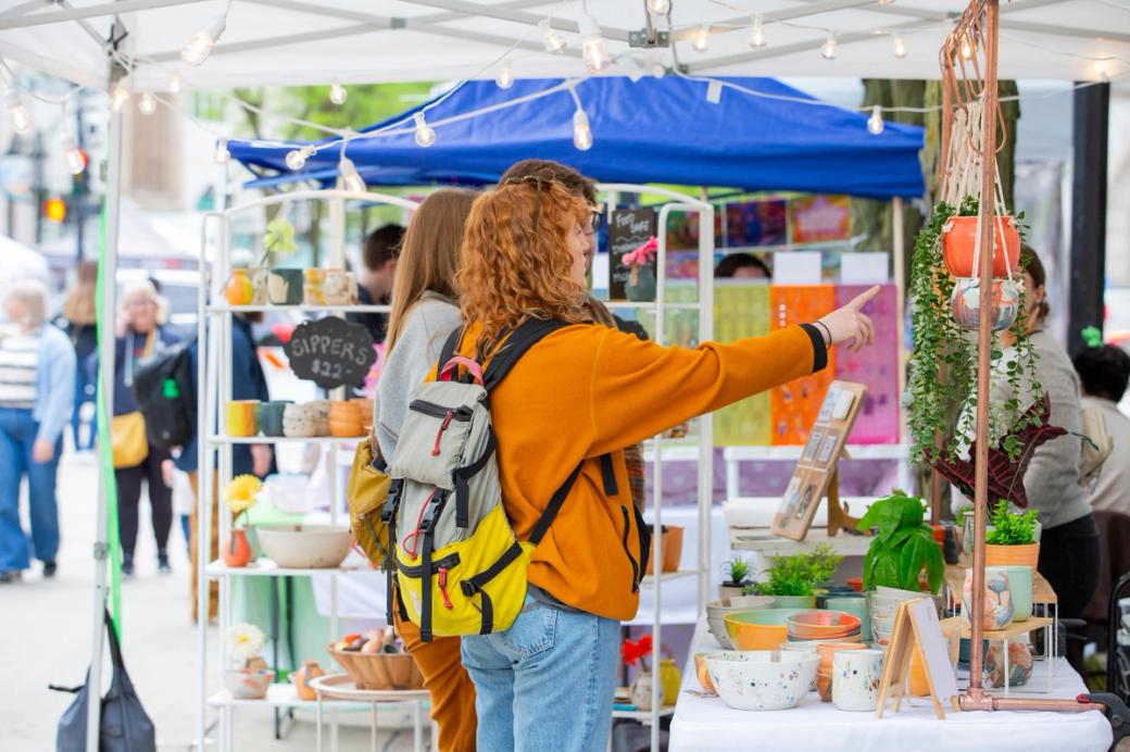 A red-haired woman pointing to something at an outdoor fair.