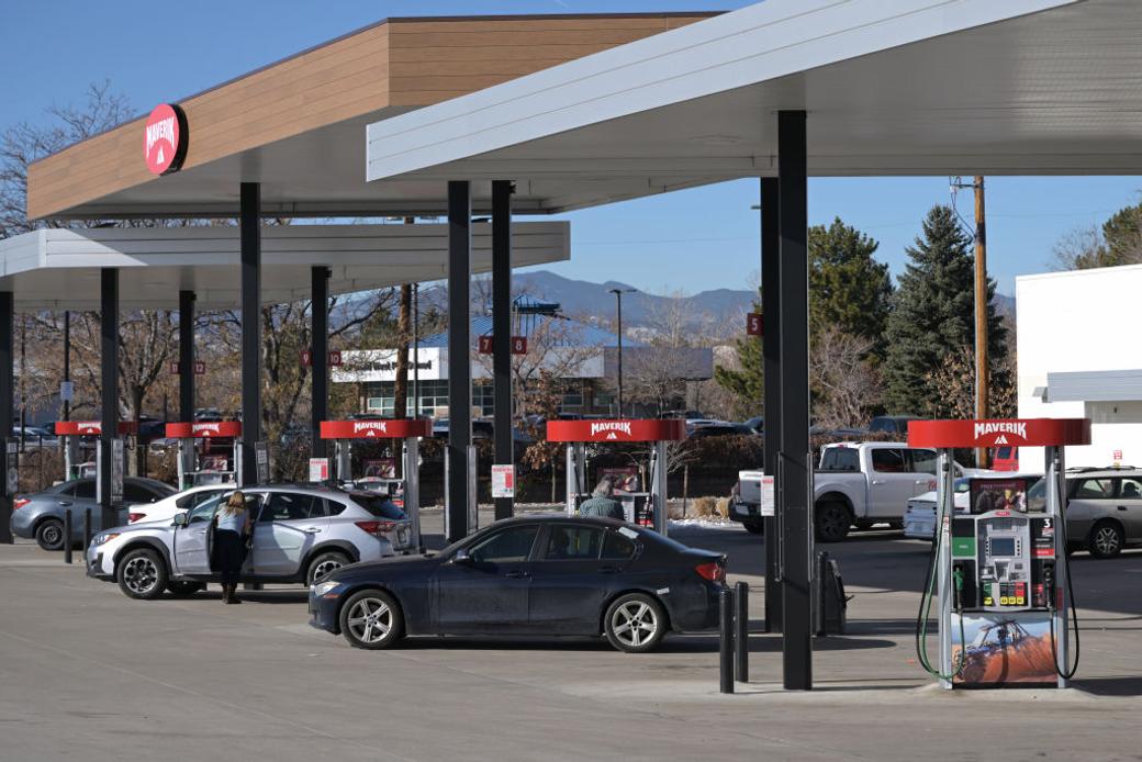 Cars lined up at a gas station to re-fuel with mountains in the background