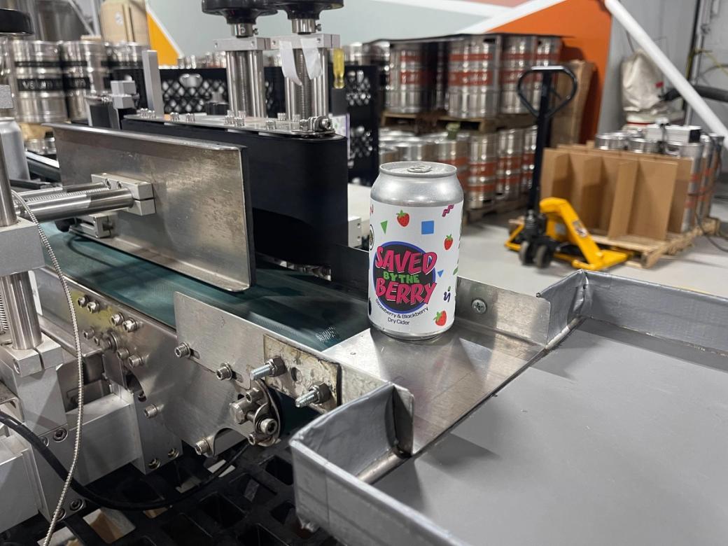 A beverage production table with a can of "Saved by the Berry" beer.