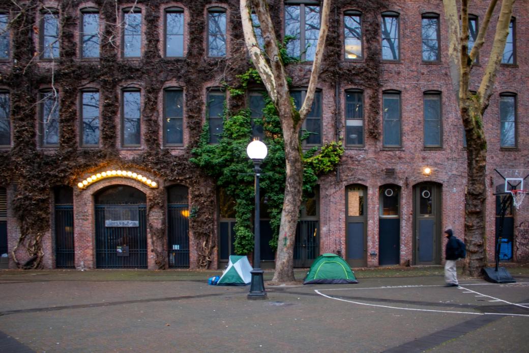 Two small green tents sit in Occidental Park in Pioneer Square, set against the backdrop of a brick building with ivy crawling up the sides.
