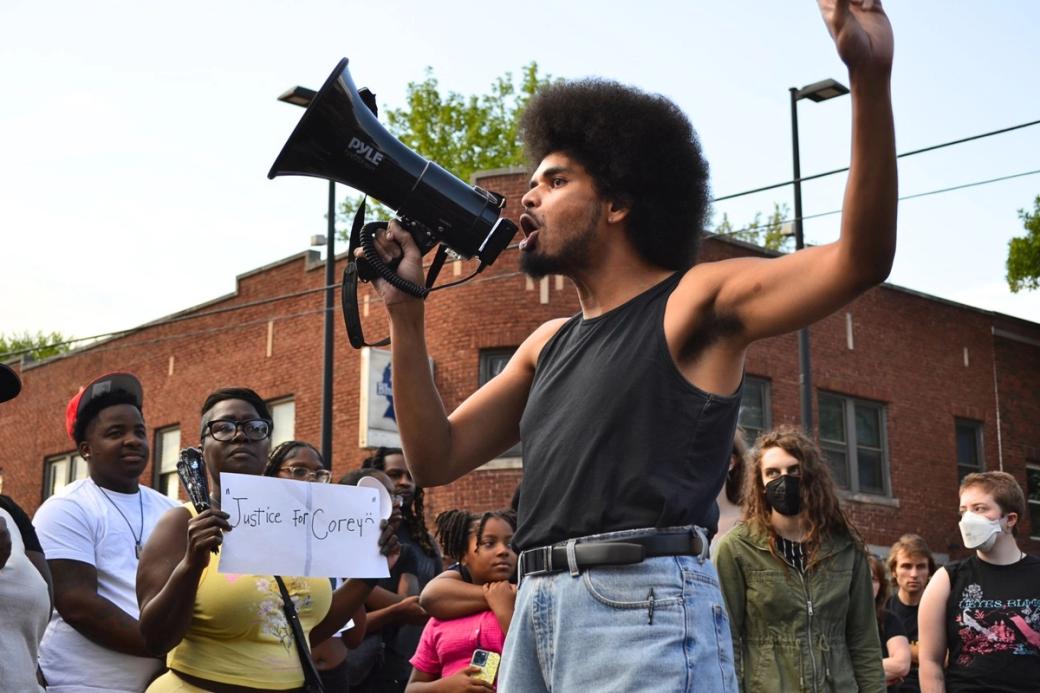 A group gathers to protest. One person talks through a megaphone.