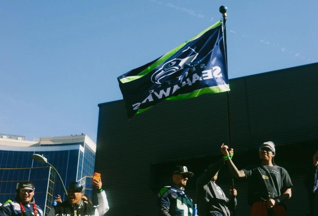 Seahawks fans celebrating the most Superbowl win stand with big smiles under the team flag at the parade downtown.