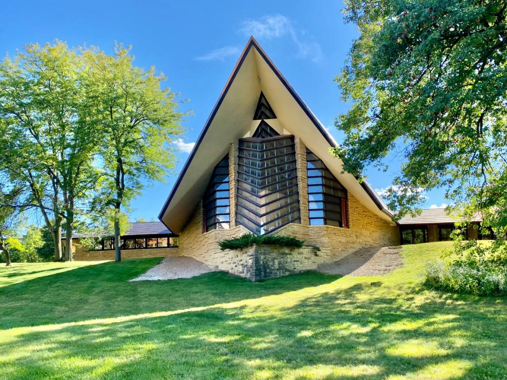 A triangular shaped building at the top of a hill of green grass.