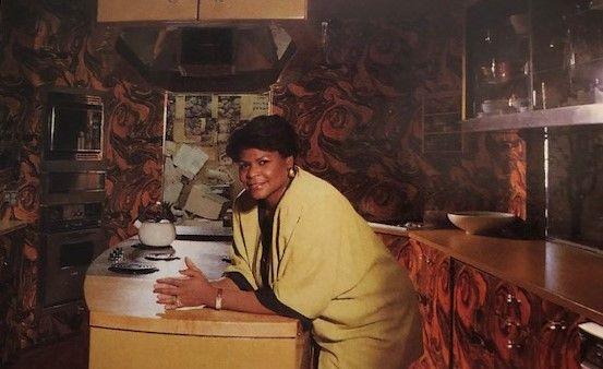 A Black woman smiles in an eclectic kitchen