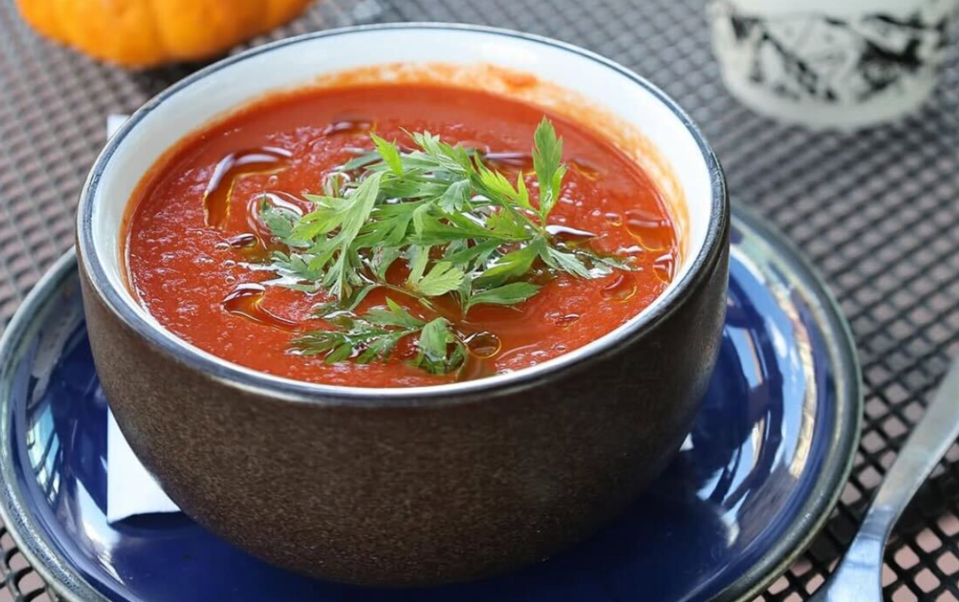 Tomato soup in a bowl on a blue plate on a table.
