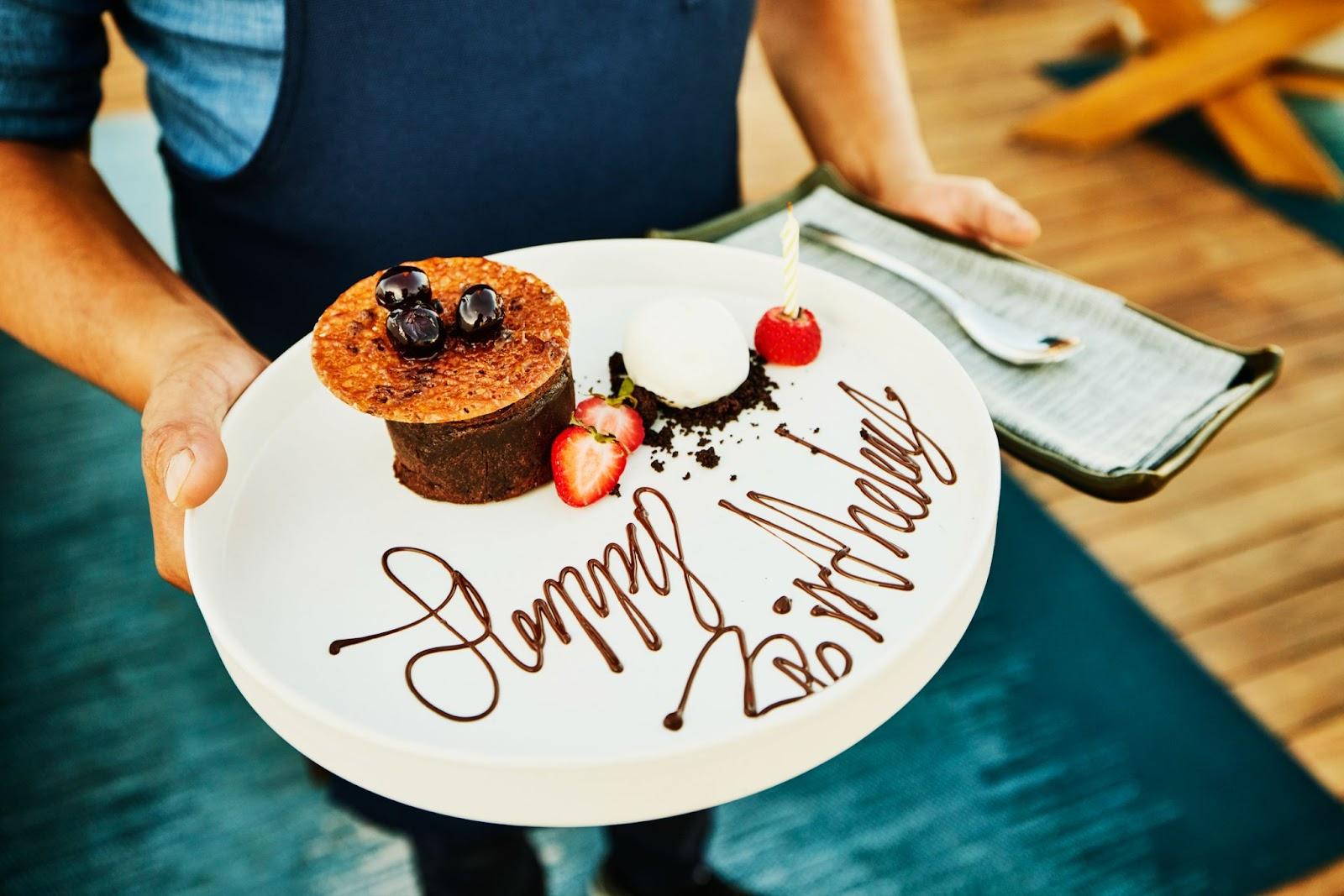 a server carries a dessert with happy birthday written on the plate in chocolate