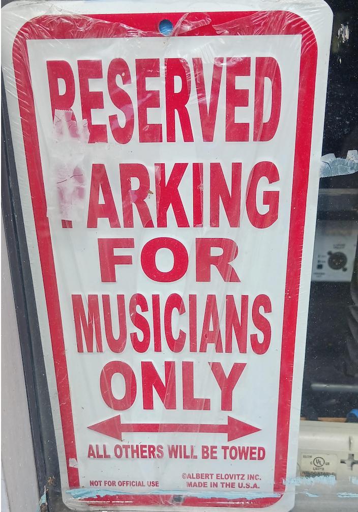 White sign with read lettering reads: “Parking for musicians only all others will be towed"