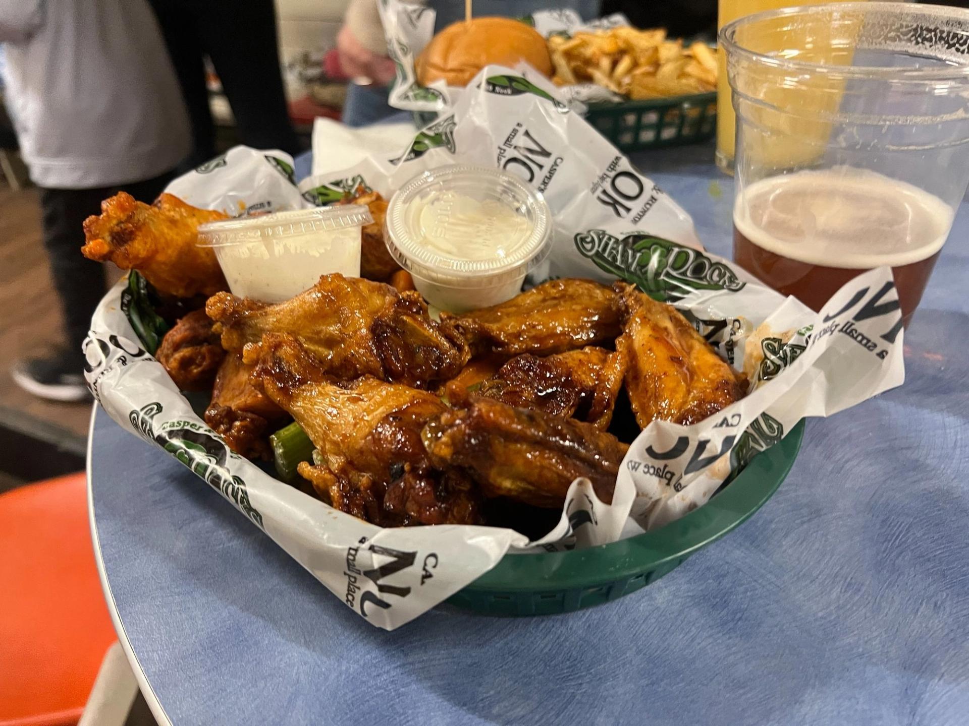 A tray of orange wings with two sides of ranch in it. There's a beer on the table next to it