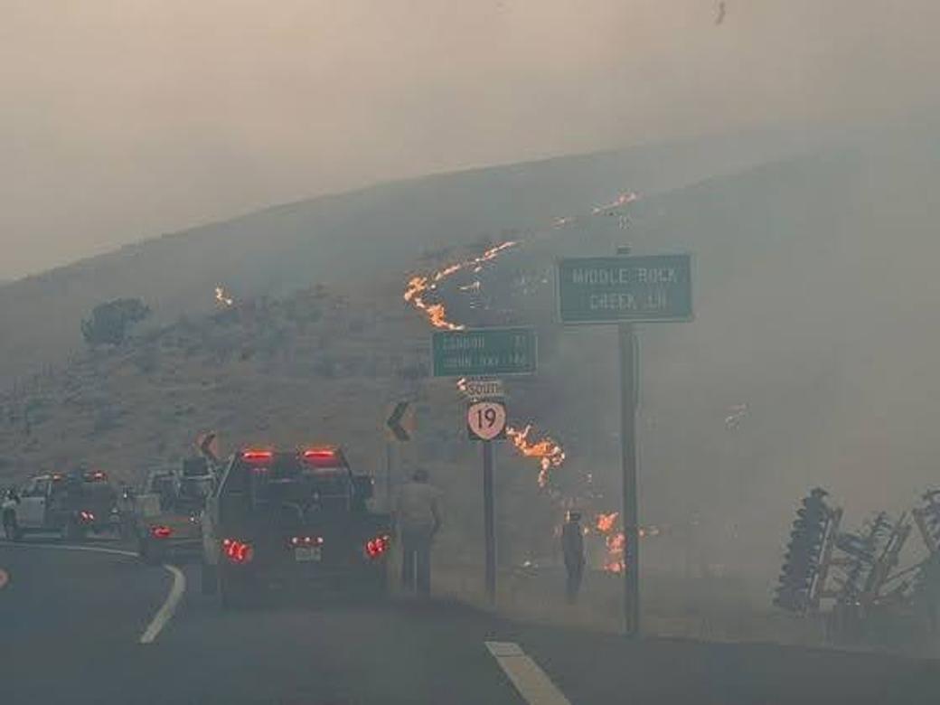 Gray air with tow tricks stopped by the side of the road. Hill on fire.