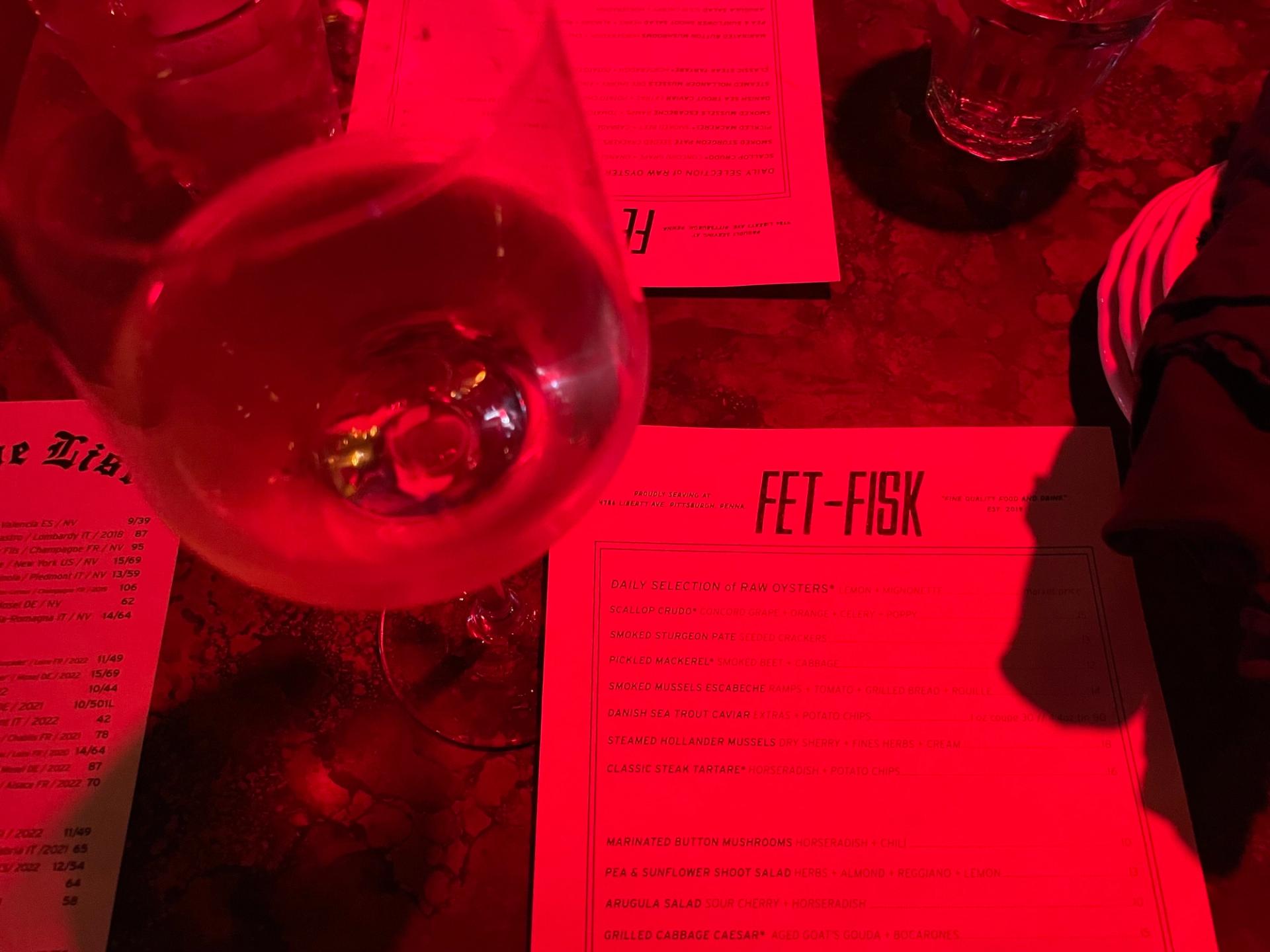 a wine glass and a menu reading "FET-FISK" at the top with red moody lighting shining on it