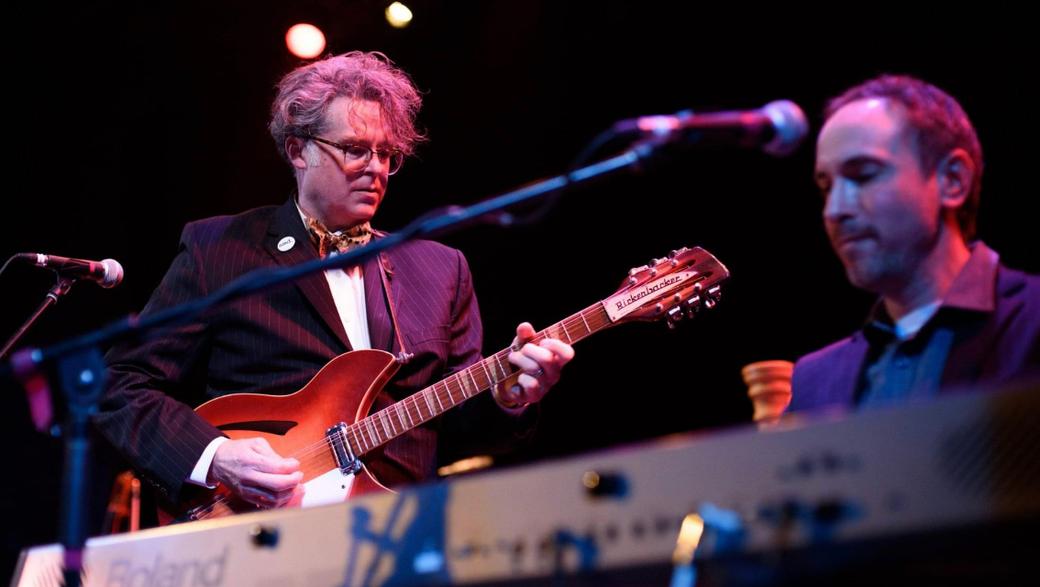 A man playing guitar behind a man playing keyboard.