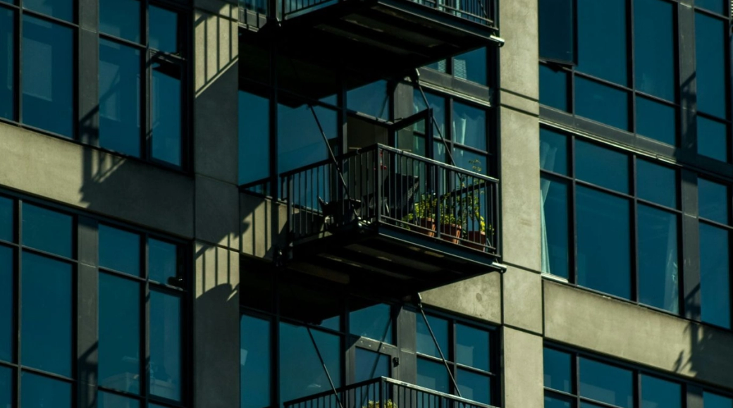 Small metal balconies sit atop one another on a glass, steel and concrete apartment building.