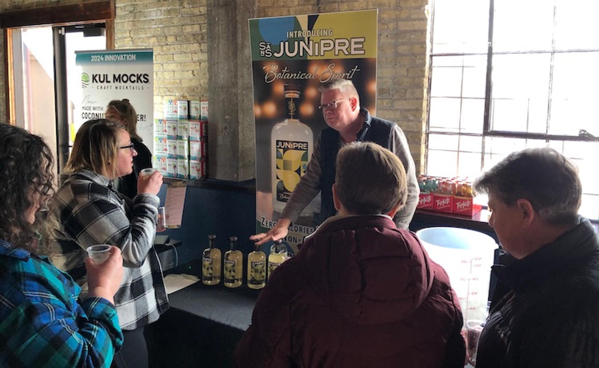A man at a table pours drink samples in small plastic glasses. 