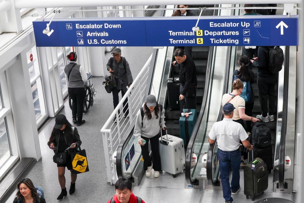 A group of people gathered around the up and down escalator at an airport.