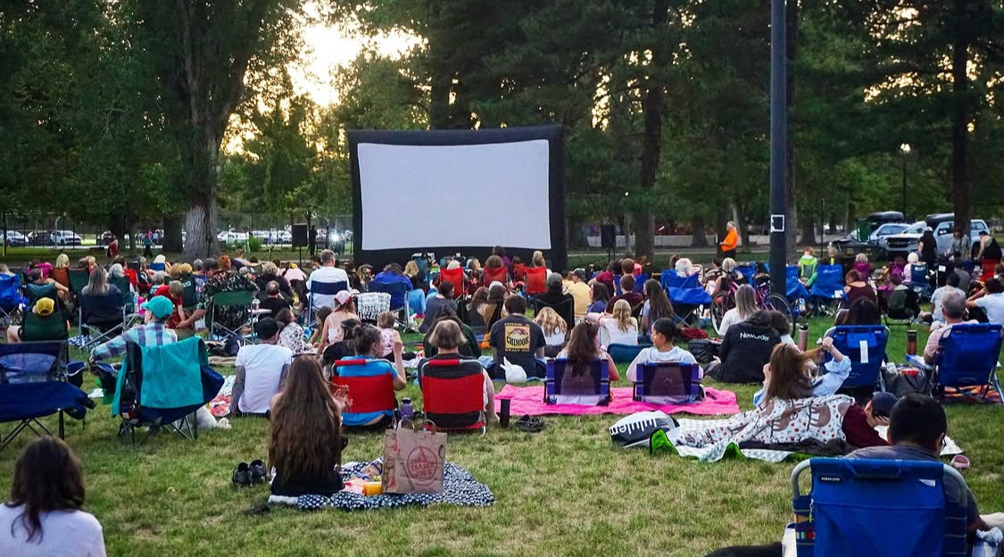 People sitting in a park in front of a large movie screen.