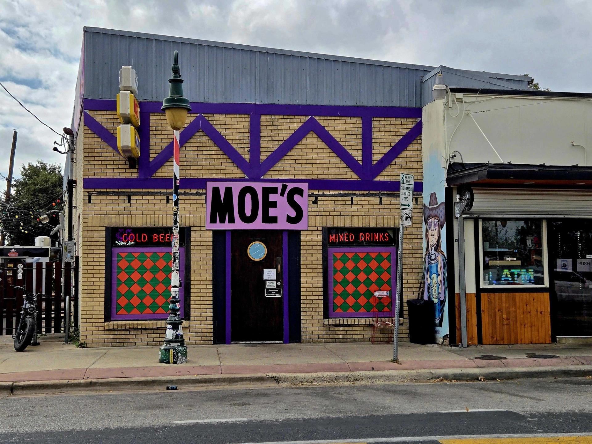 A brick building on a street with purple trim and a purple sign that says "Moe's" in black writing.