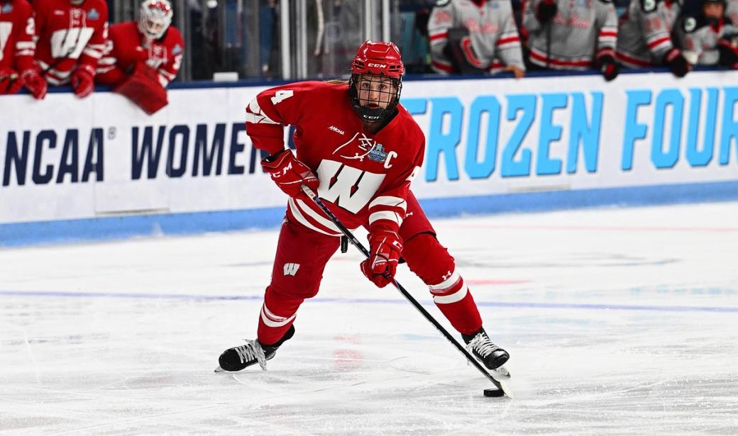Caroline KK Harvey is on ice in her UW hockey uniform mid game with a look of focus.
