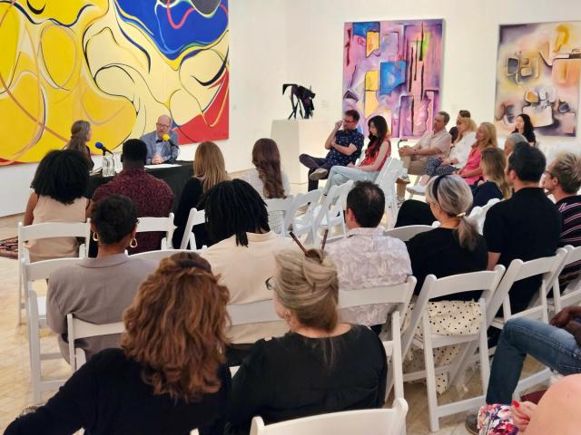 A podcast taping in front of a crowd with art in the background. 