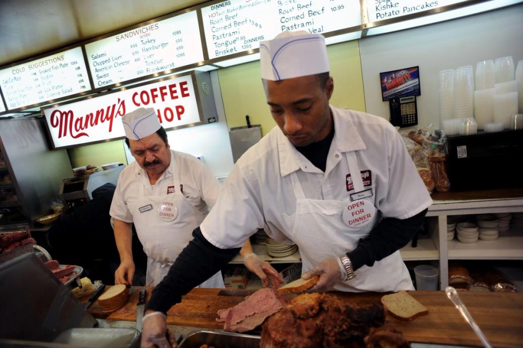 Two men behind the counter making a sandwich at a deli