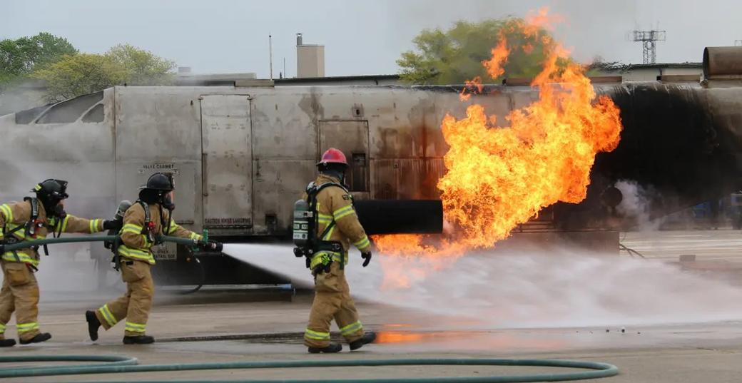 Three firefighters put our a fire using a hose on a large metal object