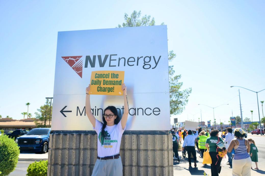 A woman holds a sign at NVEnergy headquarters. It reads "Cancel the Daily Demand Charge!"
