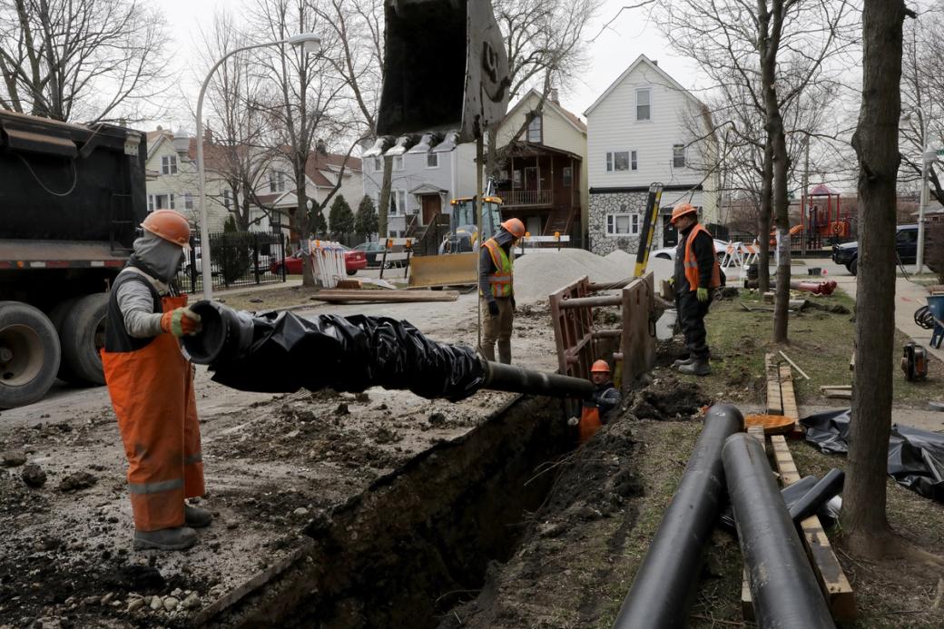 Crew wearing hi-vis orange safety apparel install large pipes into hole in ground