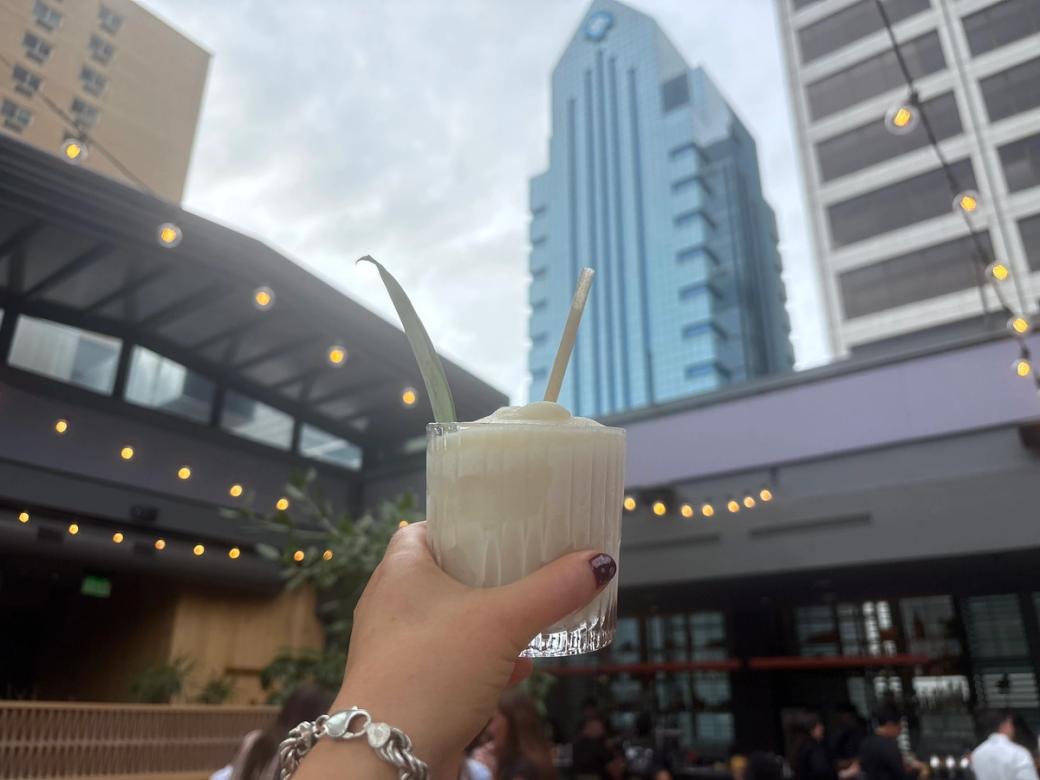 A hand holds a drink in the air, with a view of skyscrapers in the background