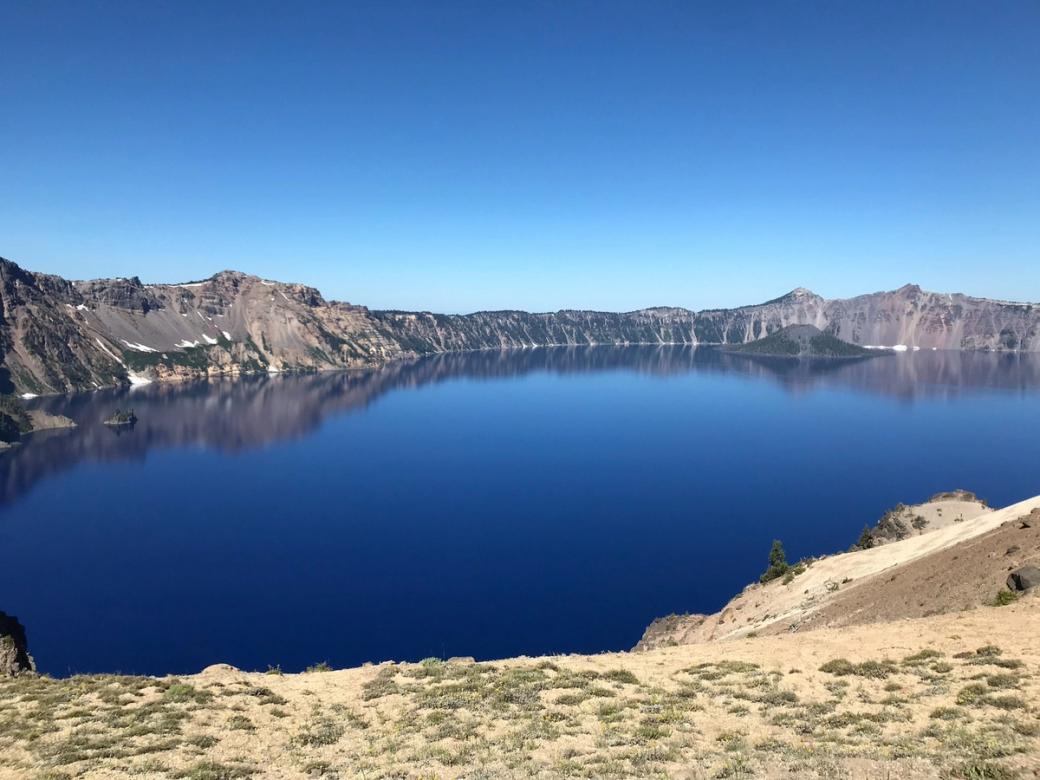 A large deep blue lake surrounded by rocky ridges under a clear blue sky. 