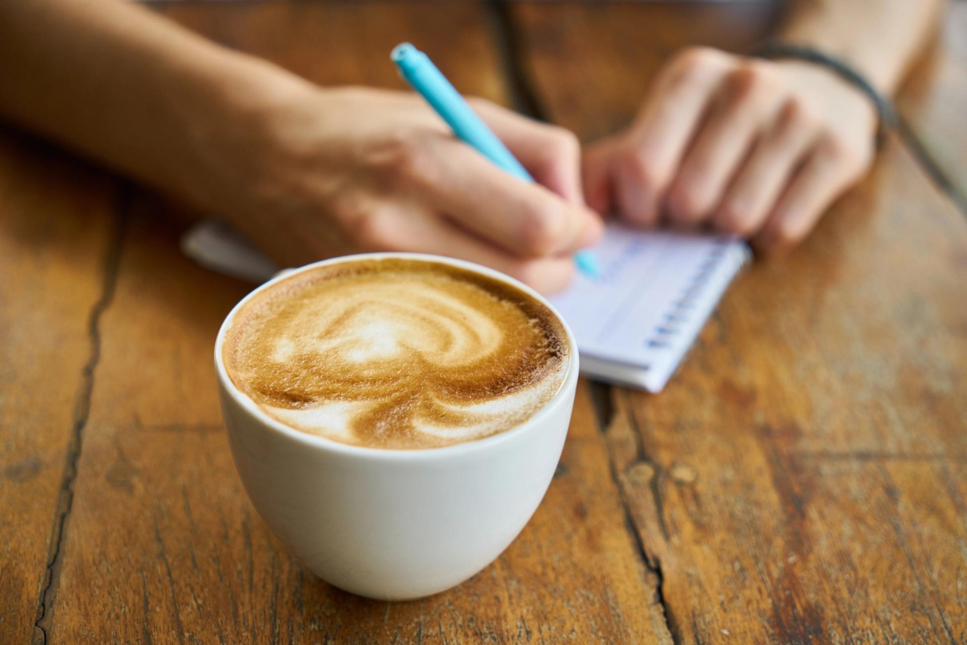 Hand writing on pad next to cup of coffee.