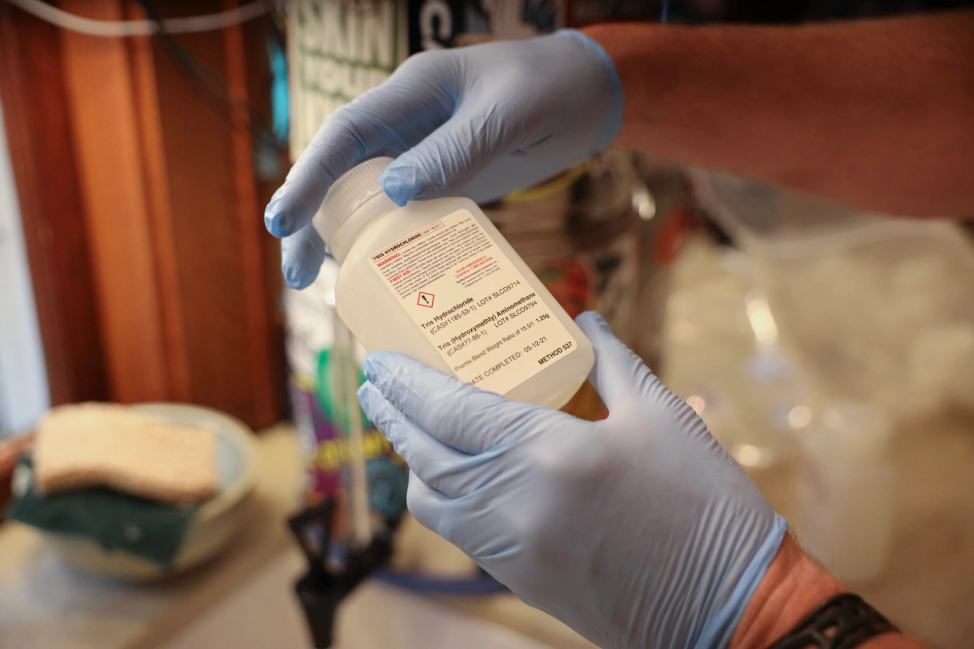 Wearing gloves and holding a clear plastic bottle, Madison, Wis., resident Brad Horn collects a water sample to test for PFAS in Madison, Wis., on Aug. 8, 2022.