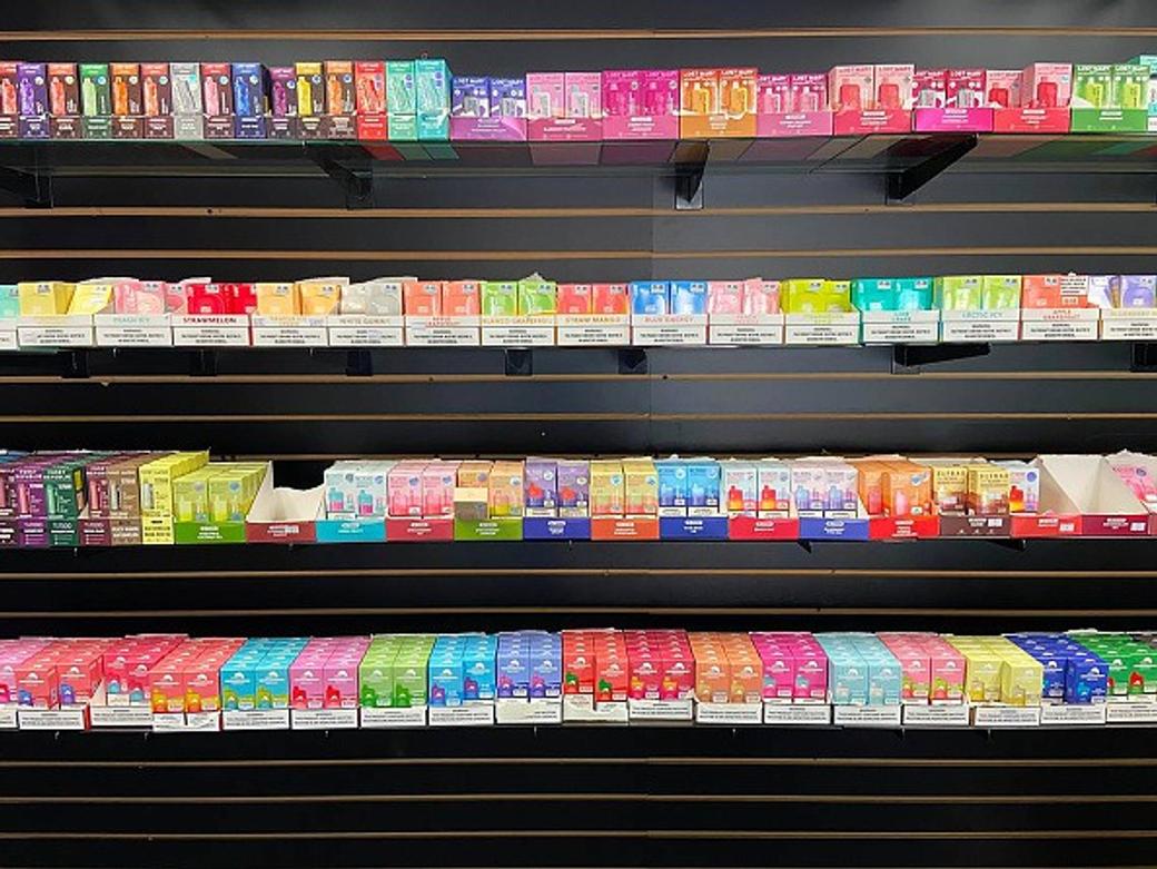 Rows of brightly colored vape products displayed on black shelves inside a store.