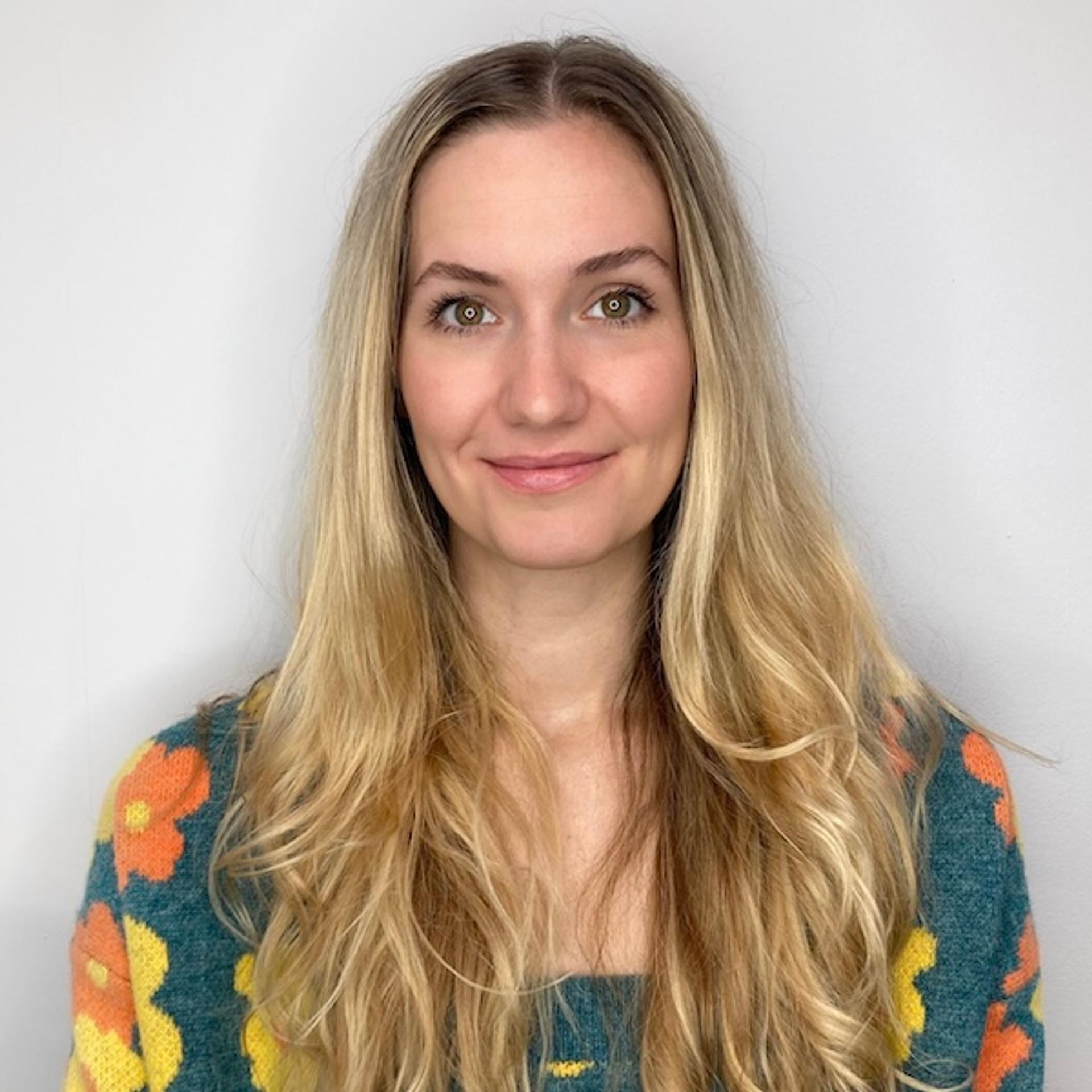 woman with long blonde hair in grey sweater with orange and yellow flowers