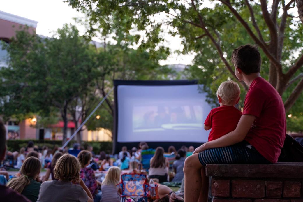 A crowd watches an outdoor movie screen. 