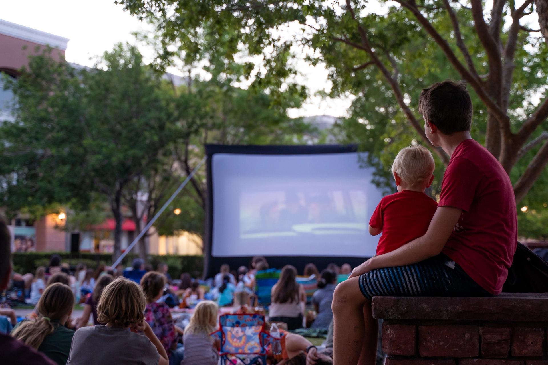 A crowd watches an outdoor movie screen.