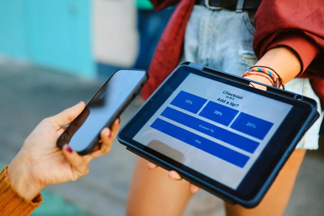a person proffers a checkout tablet displaying tipping options.
