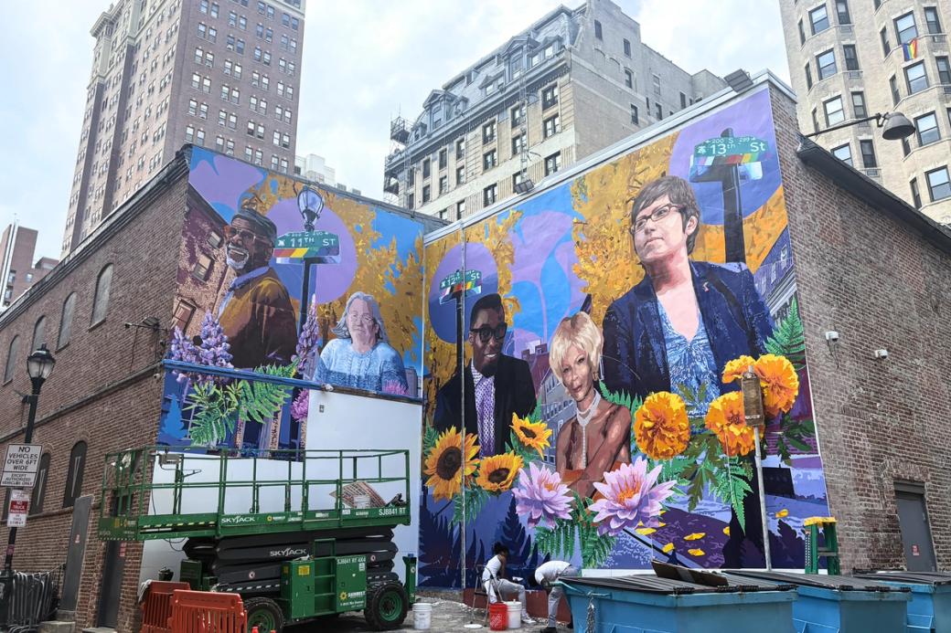 A colorful mural depicting five LGBTQ+ advocates with colorful flowers lining the bottom is being worked on by a crew of painters.