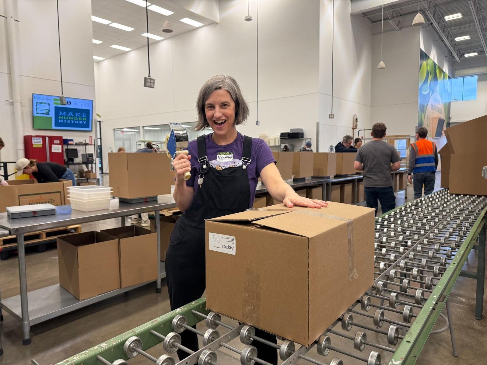 A woman in overalls and tape, packing up a box