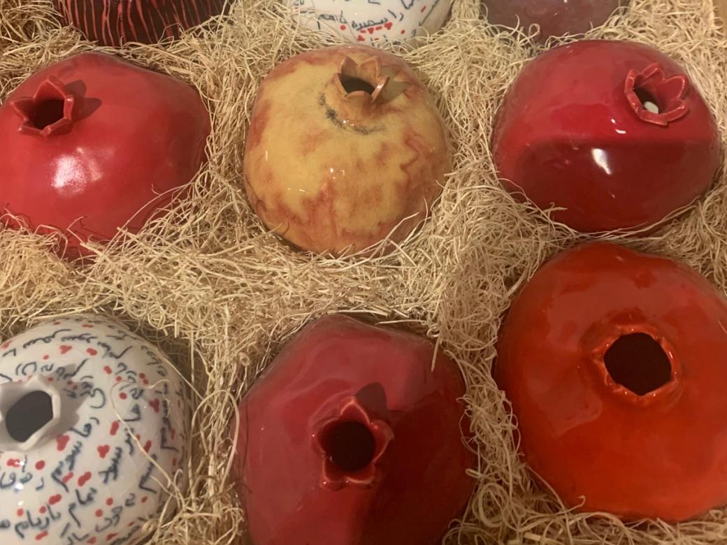 Ceramic pomegranates arranged in rows in shredded packing material that resembles hay